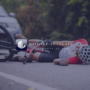 Maloney-Lyons, LLC Attorneys at Law logo over an image of a cyclist lying on the road after an accident, representing Biloxi Bicycle Accident Lawyer services.